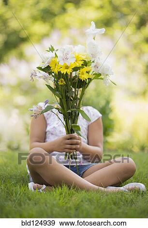 Stock Photo - Mixed race girl holding bouquet of flowers in grass. Fotosearch