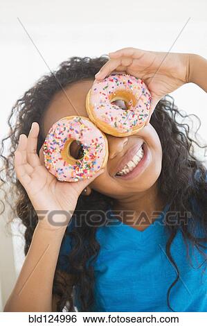 Stock Photograph - Mixed race girl holding donuts over her eyes. Fotosearch