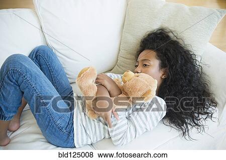 Mixed race girl hugging teddy bear on sofa View Large Photo Image Stock Photo - Mixed race girl hugging teddy bear on sofa. Fotosearch
