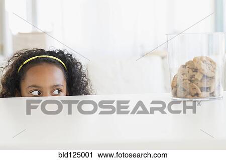 Stock Image - Mixed race girl peering at cookie jar. Fotosearch