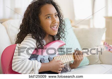 Stock Photo - Mixed race girl playing electric guitar on sofa. Fotosearch