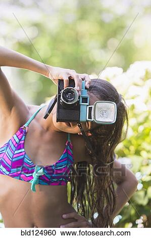Stock Image - Mixed race girl taking pictures with toy camera outdoors. Fotosearch