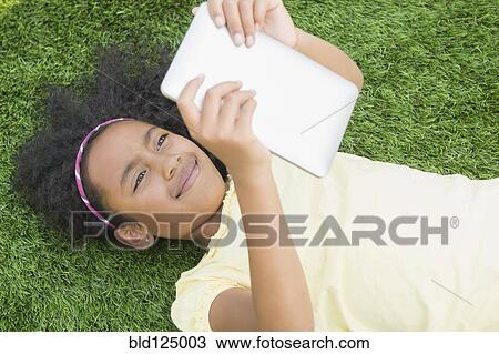 Stock Image - Mixed race girl using digital tablet in grass. Fotosearch