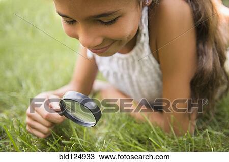 Stock Image - Mixed race girl using magnifying glass in grass. Fotosearch