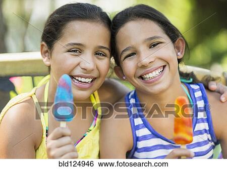 Stock Photograph - Mixed race girls eating flavored ice outdoors. Fotosearch