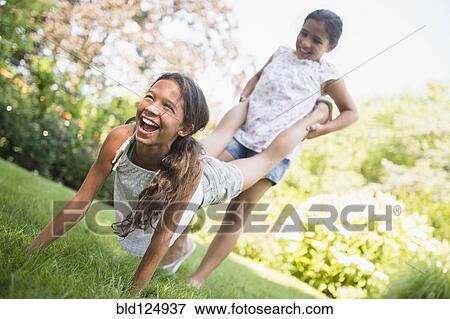Stock Photo - Mixed race girls playing wheelbarrow in backyard. Fotosearch