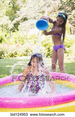 Stock Image - Mixed race girls splashing in wading pool. Fotosearch