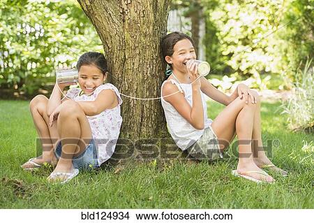 Picture - Mixed race girls talking into tin can telephones outdoors. Fotosearch