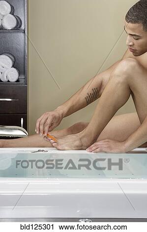 Stock Image - Mixed race man filing his toenails at bathtub. Fotosearch