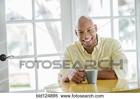 Stock Photography - Mixed race man having coffee in kitchen. Fotosearch