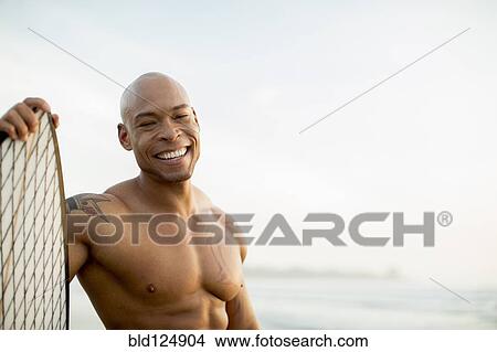 Mixed race man holding surfboard on beach View Large Photo Image Picture - Mixed race man holding surfboard on beach. Fotosearch