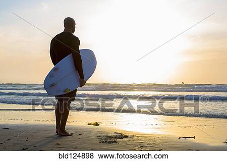 Mixed race man holding surfboard on beach View Large Photo Image Stock Photo - Mixed race man holding surfboard on beach. Fotosearch
