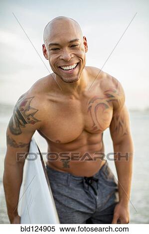 Stock Photography - Mixed race man holding surfboard on beach. Fotosearch