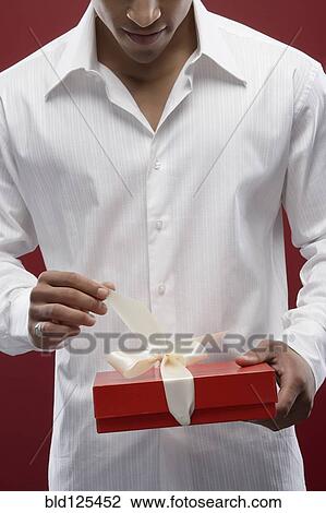Stock Image - Mixed race man opening wrapped gift. Fotosearch