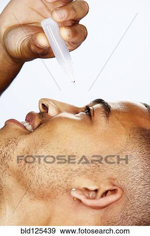 Stock Photo - Mixed race man putting in eye drops. Fotosearch