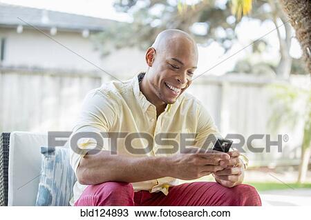 Stock Image - Mixed race man using cell phone in backyard. Fotosearch