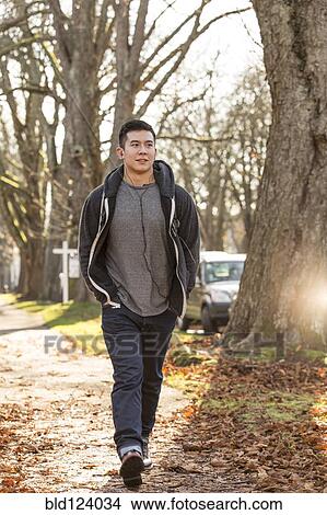 Picture - Mixed race man walking on suburban street. Fotosearch