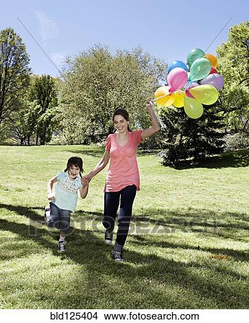 Mixed race mother and daughter holding balloons in park View Large Photo Image Picture - Mixed race mother and daughter holding balloons in park. Fotosearch