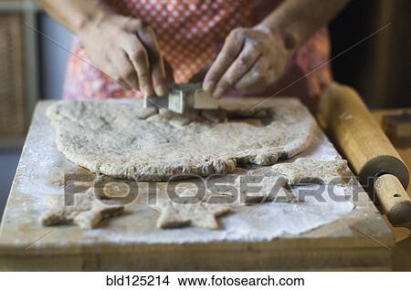 Picture - Mixed race woman cutting cookie dough in kitchen. Fotosearch