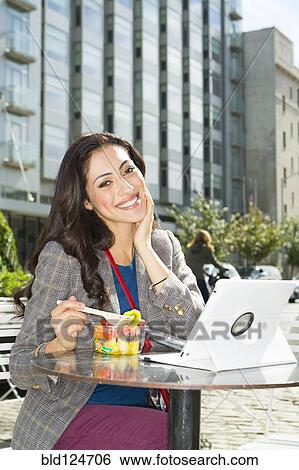 Stock Photograph - Mixed race woman eating lunch at urban sidewalk cafe. Fotosearch