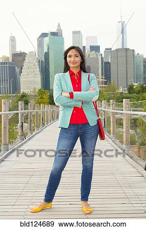 Stock Photo - Mixed race woman on footbridge in front of city skyline, New York, New York, United States. Fotosearch