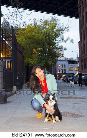 Stock Image - Mixed race woman petting dog on city sidewalk. Fotosearch