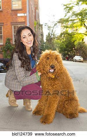 Stock Photo - Mixed race woman petting dog on city street. Fotosearch