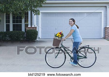 Stock Photo - Mixed race woman riding bicycle in driveway. Fotosearch