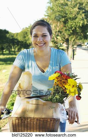 Mixed race woman riding bicycle with flowers in basket View Large Photo Image Stock Image - Mixed race woman riding bicycle with flowers in basket. Fotosearch