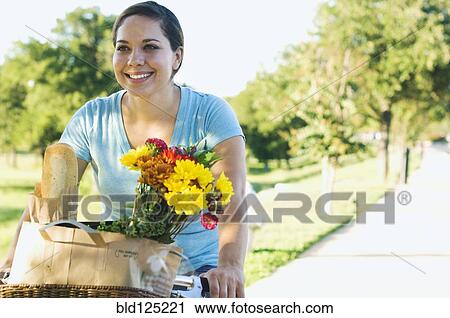 Mixed race woman riding bicycle with flowers in basket View Large Photo Image Stock Image - Mixed race woman riding bicycle with flowers in basket. Fotosearch