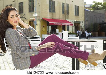Stock Image - Mixed race woman sitting at urban sidewalk cafe. Fotosearch