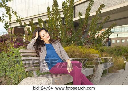 Picture - Mixed race woman sitting on park bench. Fotosearch
