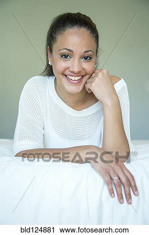 Stock Image - Mixed race woman smiling on bed. Fotosearch