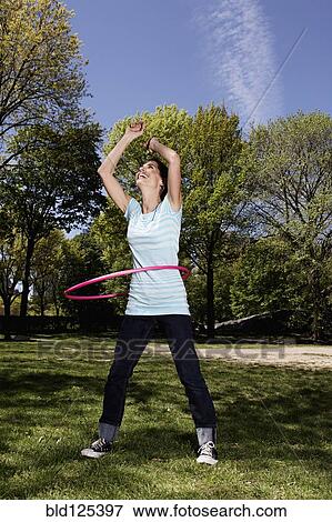 Stock Photo - Mixed race woman spinning with plastic hoop in park. Fotosearch