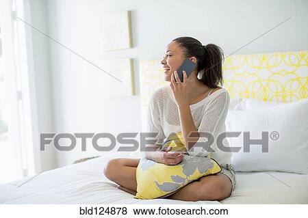 Mixed race woman talking on cell phone on bed View Large Photo Image Stock Photo - Mixed race woman talking on cell phone on bed. Fotosearch