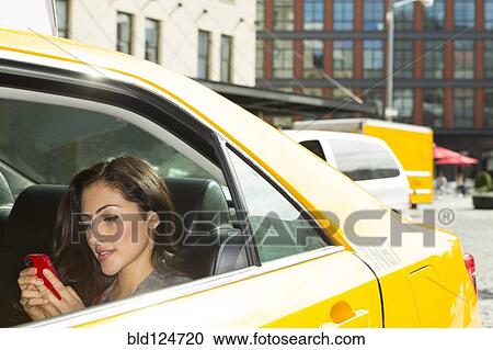 Stock Image - Mixed race woman using cell phone in taxi. Fotosearch