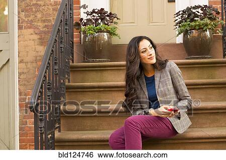 Stock Photograph - Mixed race woman using cell phone on front stoop. Fotosearch