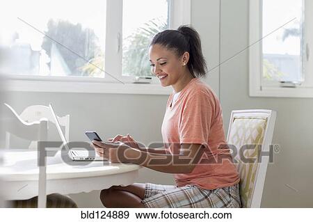 Mixed race woman using laptop and cell phone at table View Large Photo Image Stock Photo - Mixed race woman using laptop and cell phone at table. Fotosearch