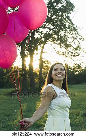 Mixed race woman with pink balloons in park View Large Photo Image Picture - Mixed race woman with pink balloons in park. Fotosearch