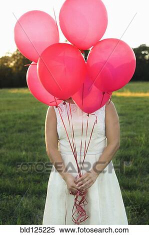 Stock Photography - Mixed race woman with pink balloons in park. Fotosearch