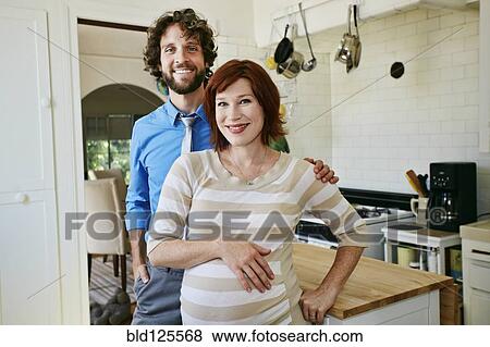 Pregnant Caucasian couple smiling in kitchen View Large Photo Image Stock Photo - Pregnant Caucasian couple smiling in kitchen. Fotosearch
