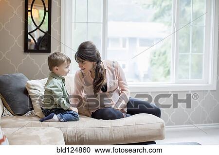 Stock Image - Pregnant Caucasian mother sitting with son in living room. Fotosearch