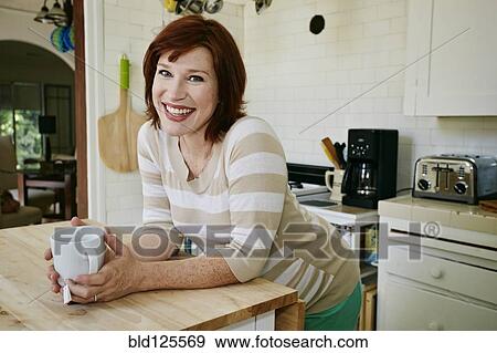Stock Photo - Pregnant Caucasian woman drinking cup of tea in kitchen. Fotosearch