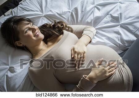 Stock Photograph - Pregnant Caucasian woman laying on bed. Fotosearch