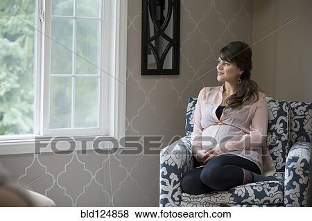 Stock Photo - Pregnant Caucasian woman sitting in living room. Fotosearch