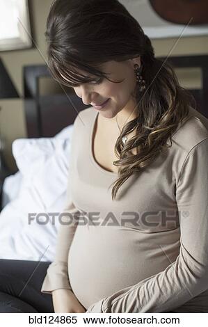 Stock Photography - Pregnant Caucasian woman sitting on bed. Fotosearch