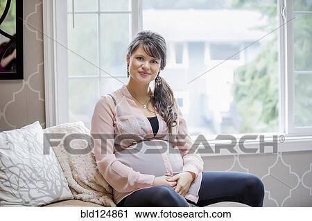 Stock Image - Pregnant Caucasian woman sitting on sofa. Fotosearch