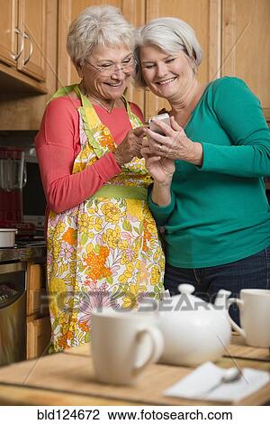 Stock Image - Senior Caucasian women using cell phone in kitchen. Fotosearch