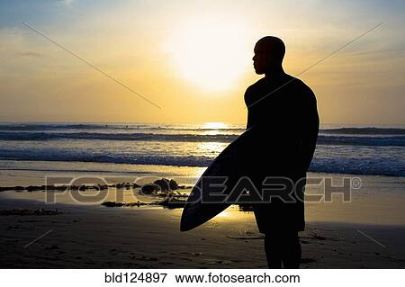 Stock Photo - Silhouette of mixed race man holding surfboard on beach. Fotosearch