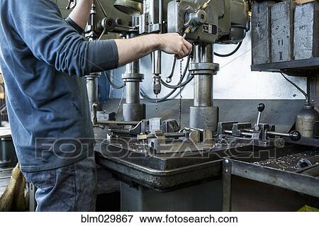 Stock Photo - Caucasian man using drilling machine in workshop. Fotosearch